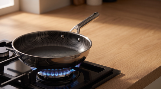 Hive Hybrid frying pan on a black gas hob grate with a ring of low blue flame beneath it